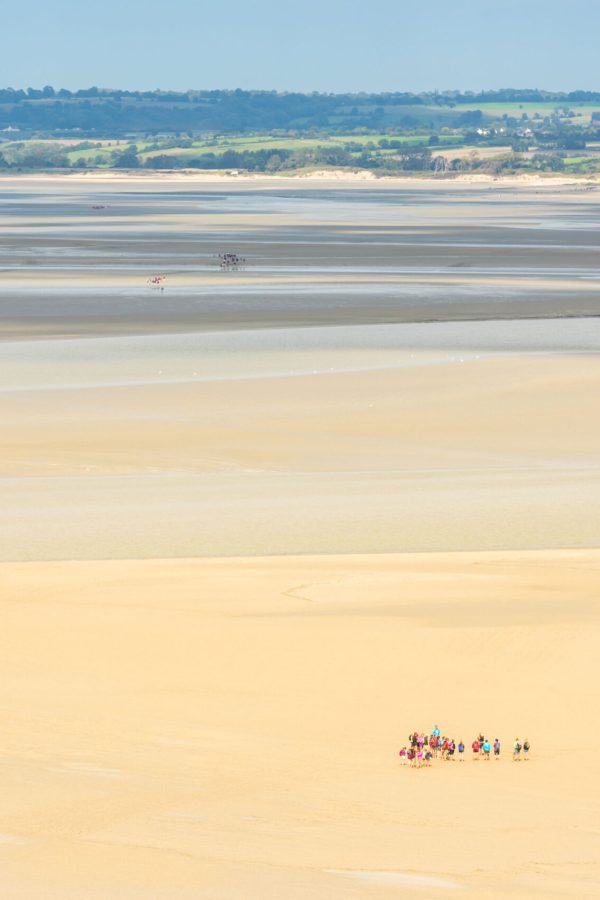 view-from-walls-of-mont-saint-michel-on-the-bay-during-the-low-tide-with-groups-of-tourists-walking-france